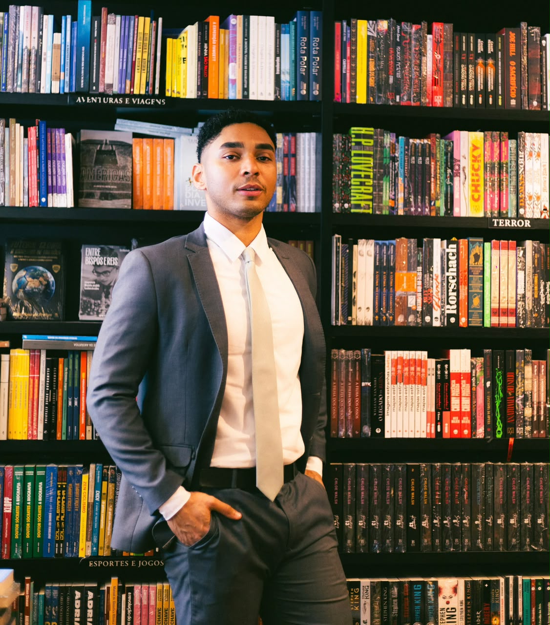 Foto colorida de Douglas Aleixo de terno diante de estantes de livros